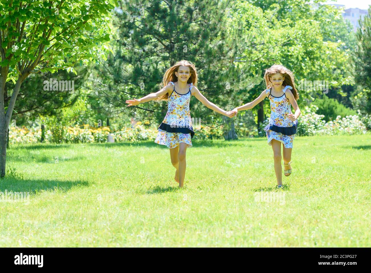 Two girls holding hands run on a green lawn in a park Stock Photo - Alamy