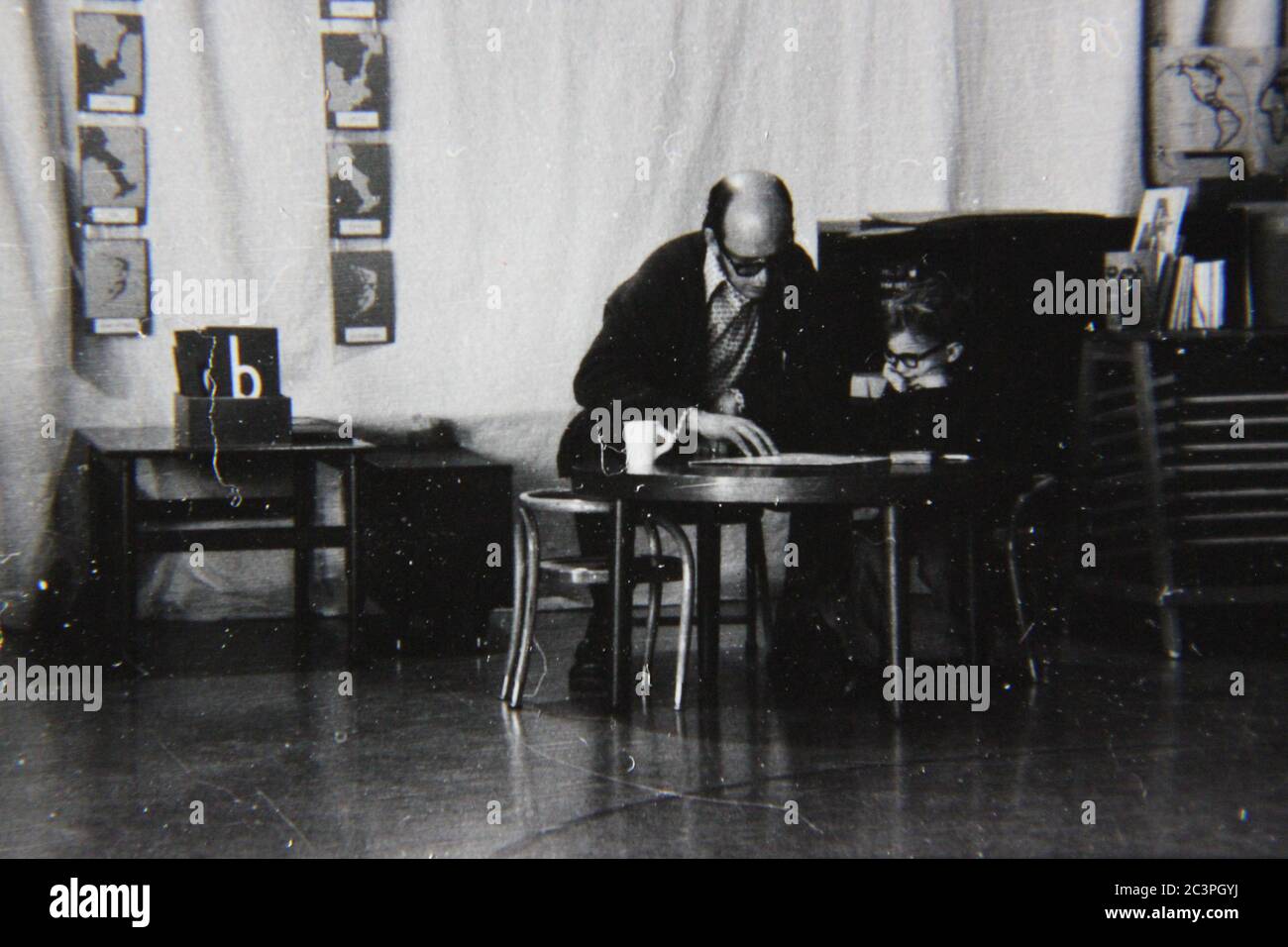 Fine 70s vintage black and white extreme photography of a man teaching a young student at a table. Stock Photo