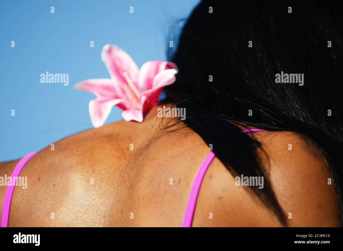 Colorful pink flower decoration resting on the shoulder of an unrecognizable young woman under bright blue sky copy space Stock Photo