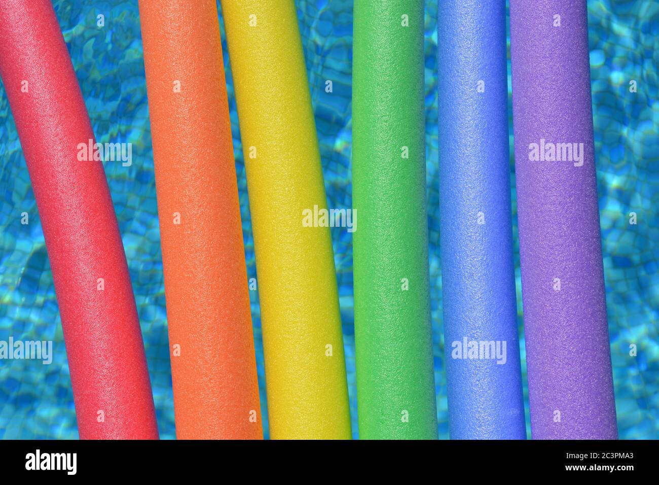 Rainbow coloured pool noodles floating in a swimming pool Stock Photo