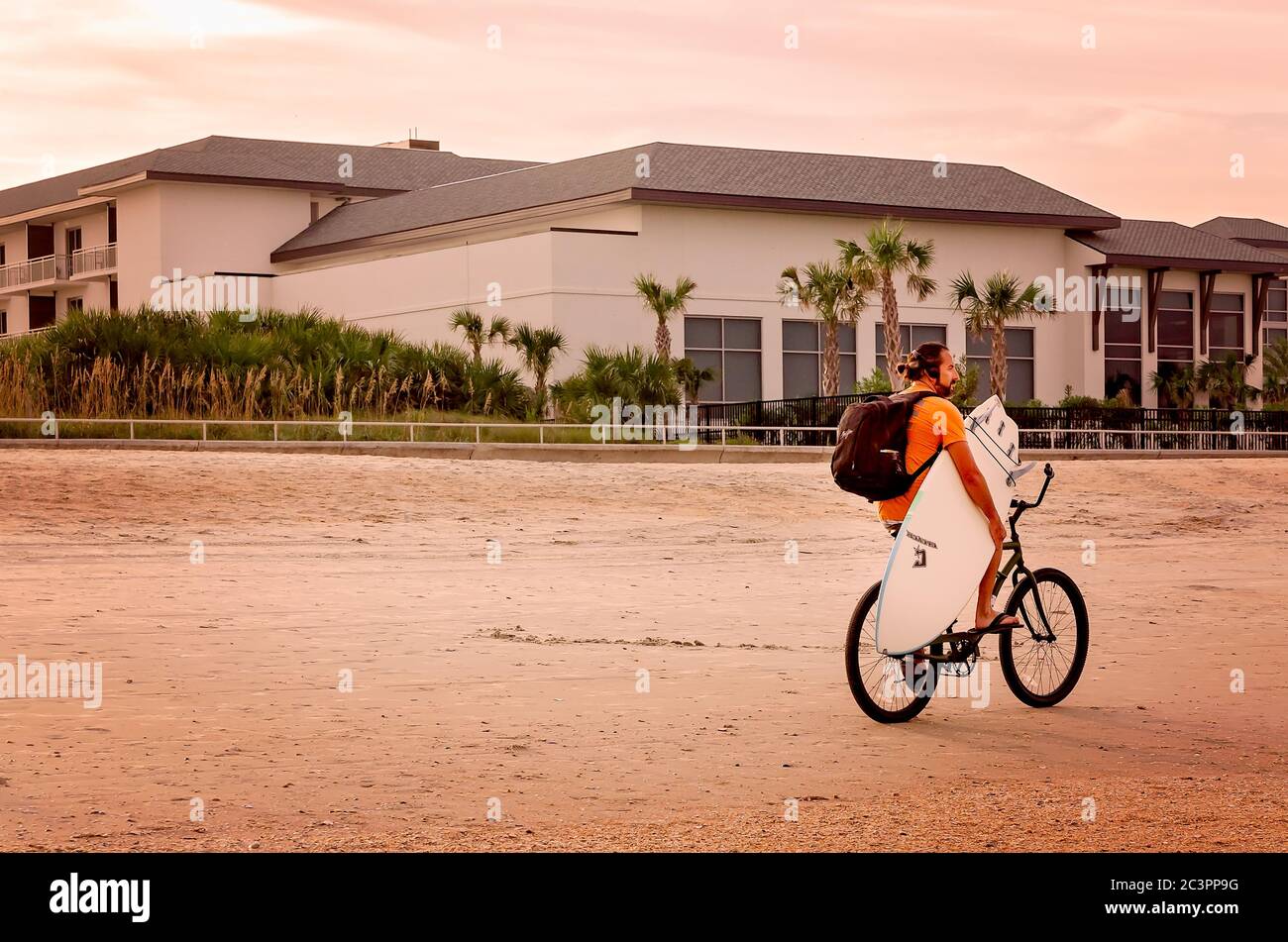 A bicyclist carries a surfboard down the beach at St. Johns County Ocean Pier, Sept. 5, 2019, in St. Augustine, Florida. Stock Photo