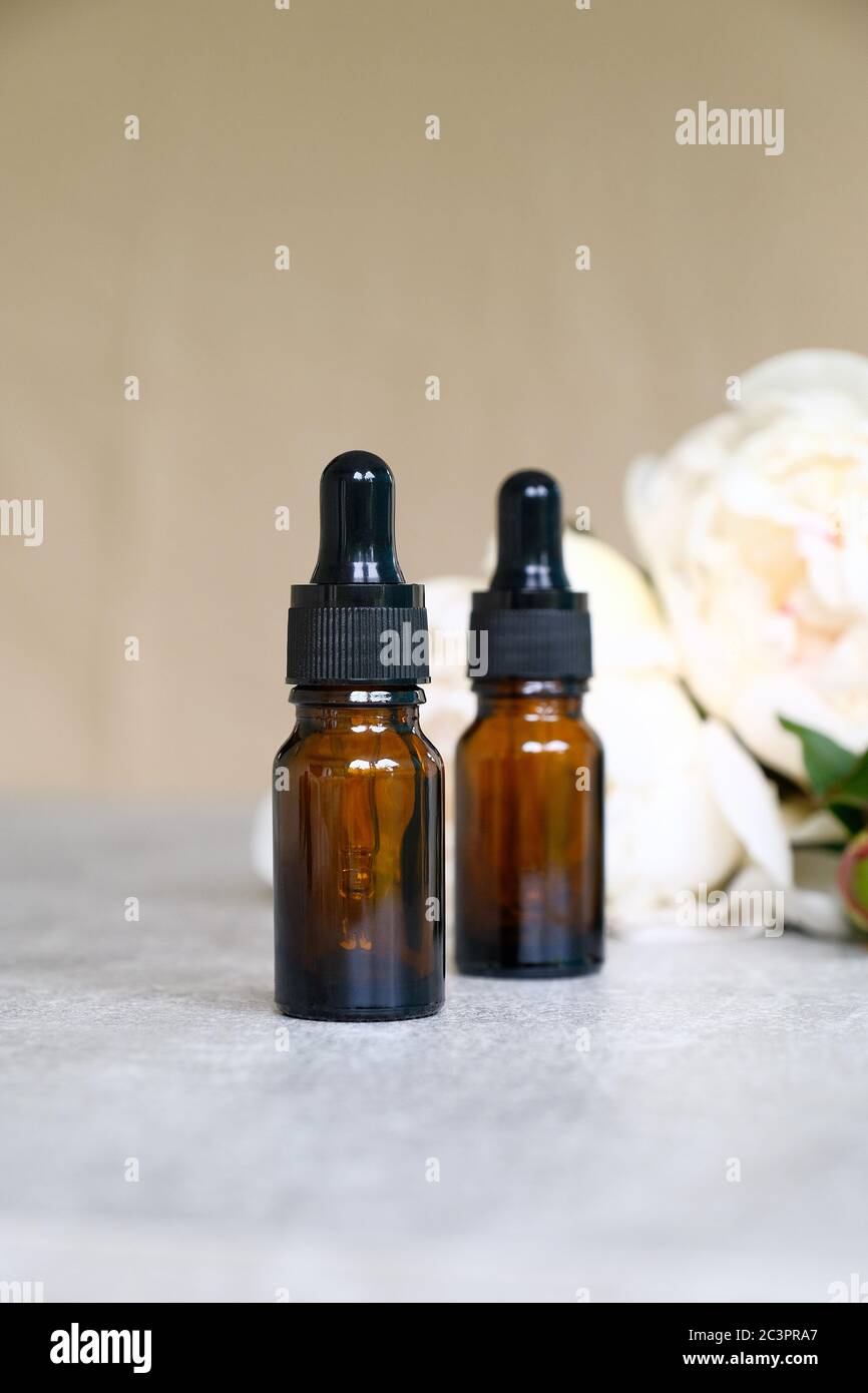 Blank amber glass dropper bottle with serum or essential oil and white peony flowers. Natural organic cosmetic concept. Stock Photo
