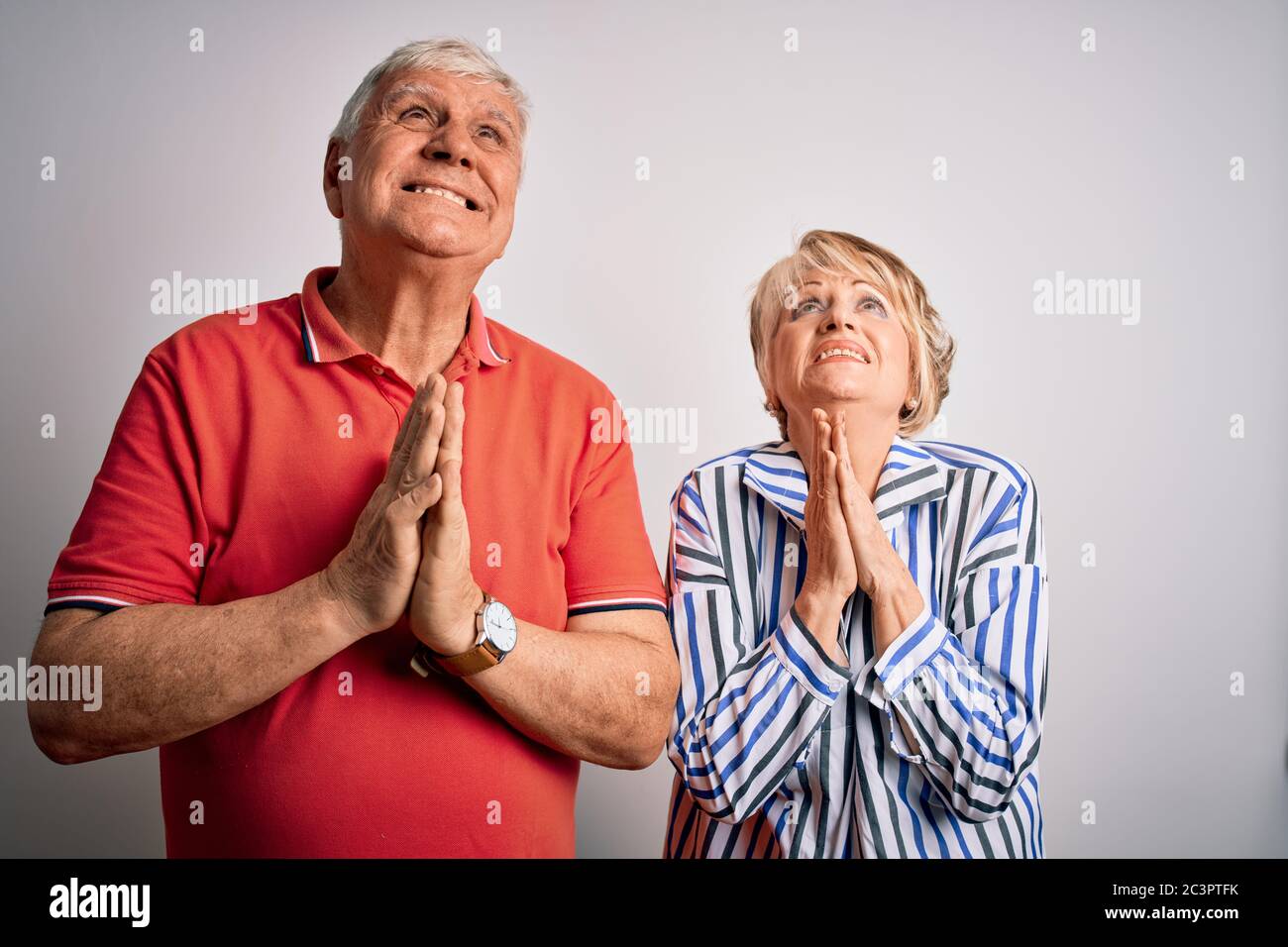 Senior beautiful couple standing together over isolated white background begging and praying with hands together with hope expression on face very emo Stock Photo