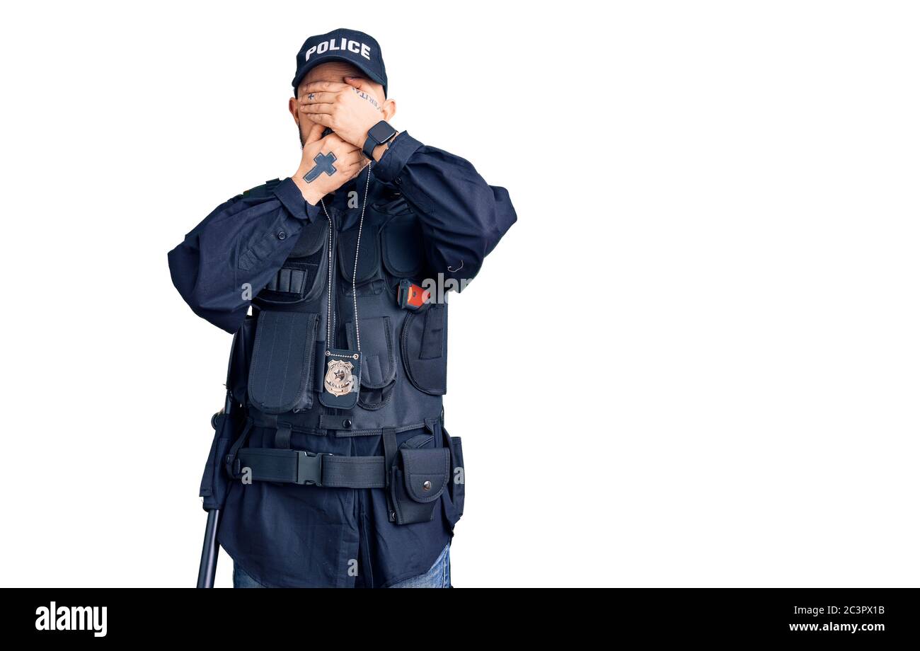 Young handsome man wearing police uniform covering eyes and mouth with hands, surprised and shocked. hiding emotion Stock Photo