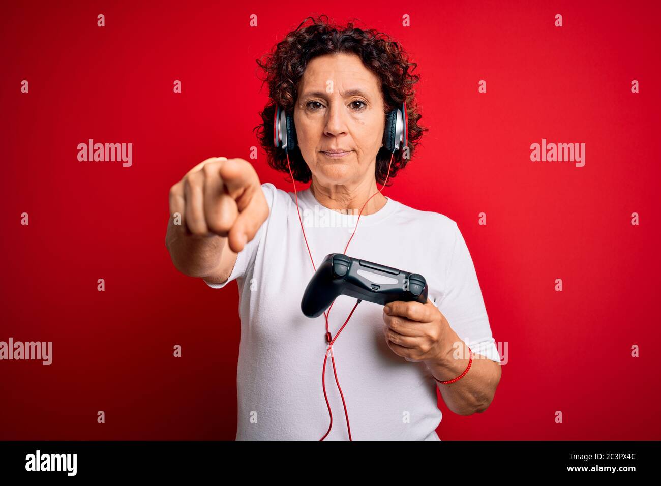 Middle age curly hair gamer woman playing video game using joystick and  headphones pointing with finger to the camera and to you, hand sign,  positive Stock Photo - Alamy