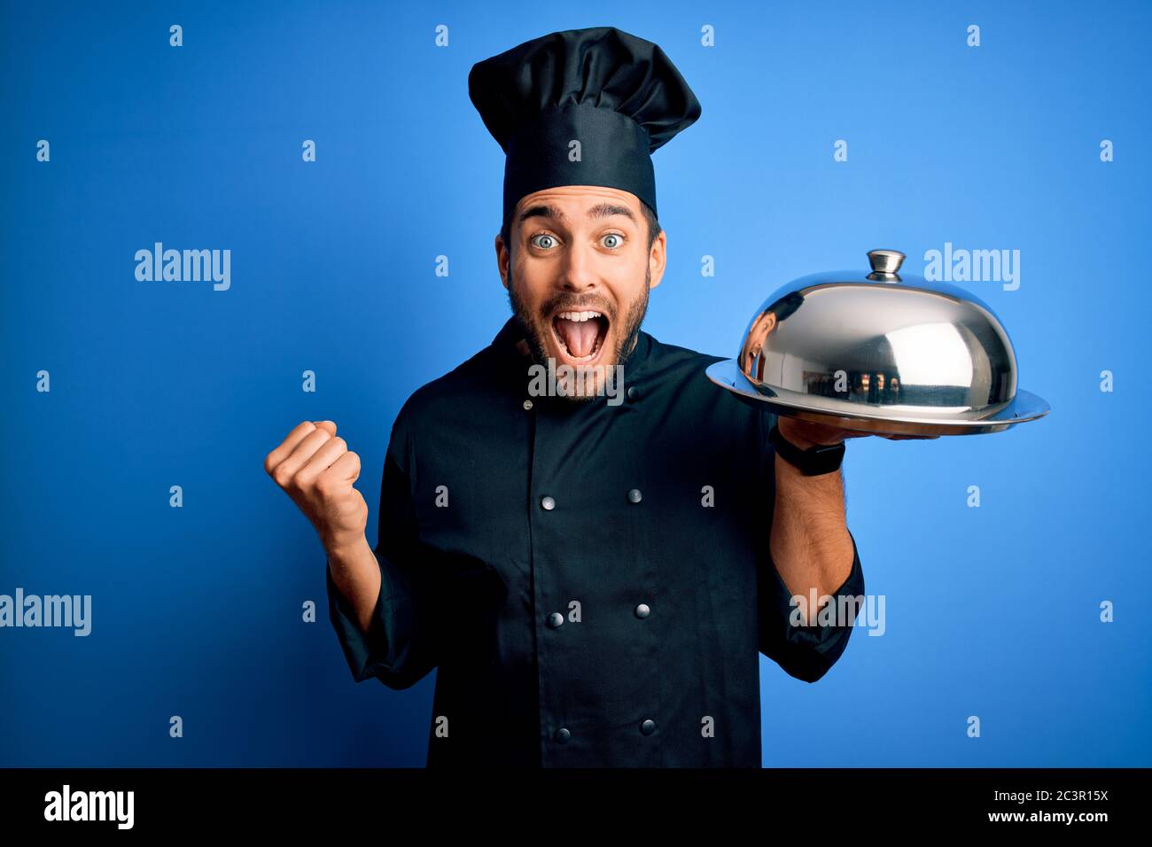 Young Cooker Man With Beard Wearing Uniform Holding Tray With Dome Over Blue Background 9790