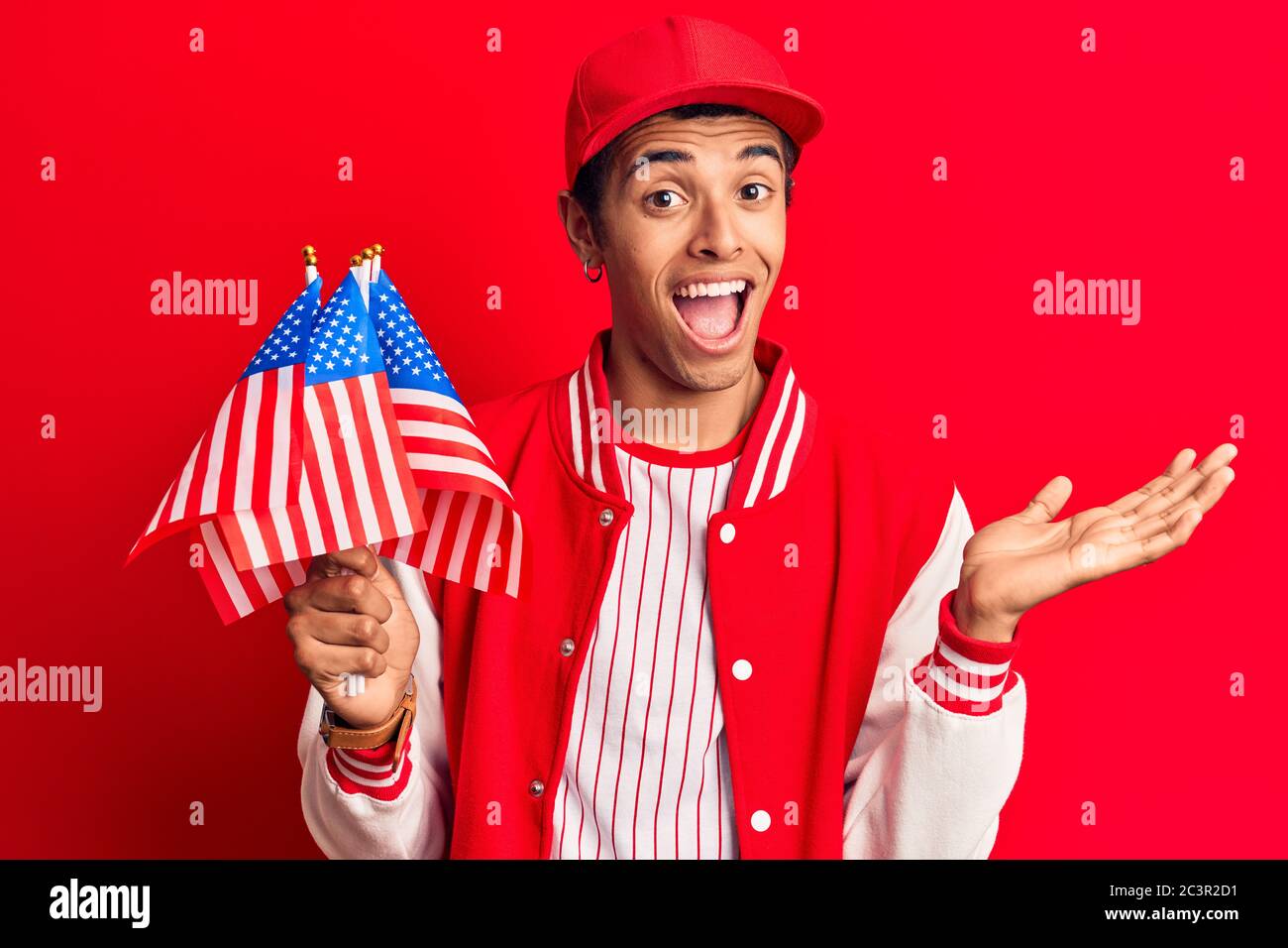 Young african amercian man wearing baseball uniform holding america flags celebrating achievement with happy smile and winner expression with raised h Stock Photo