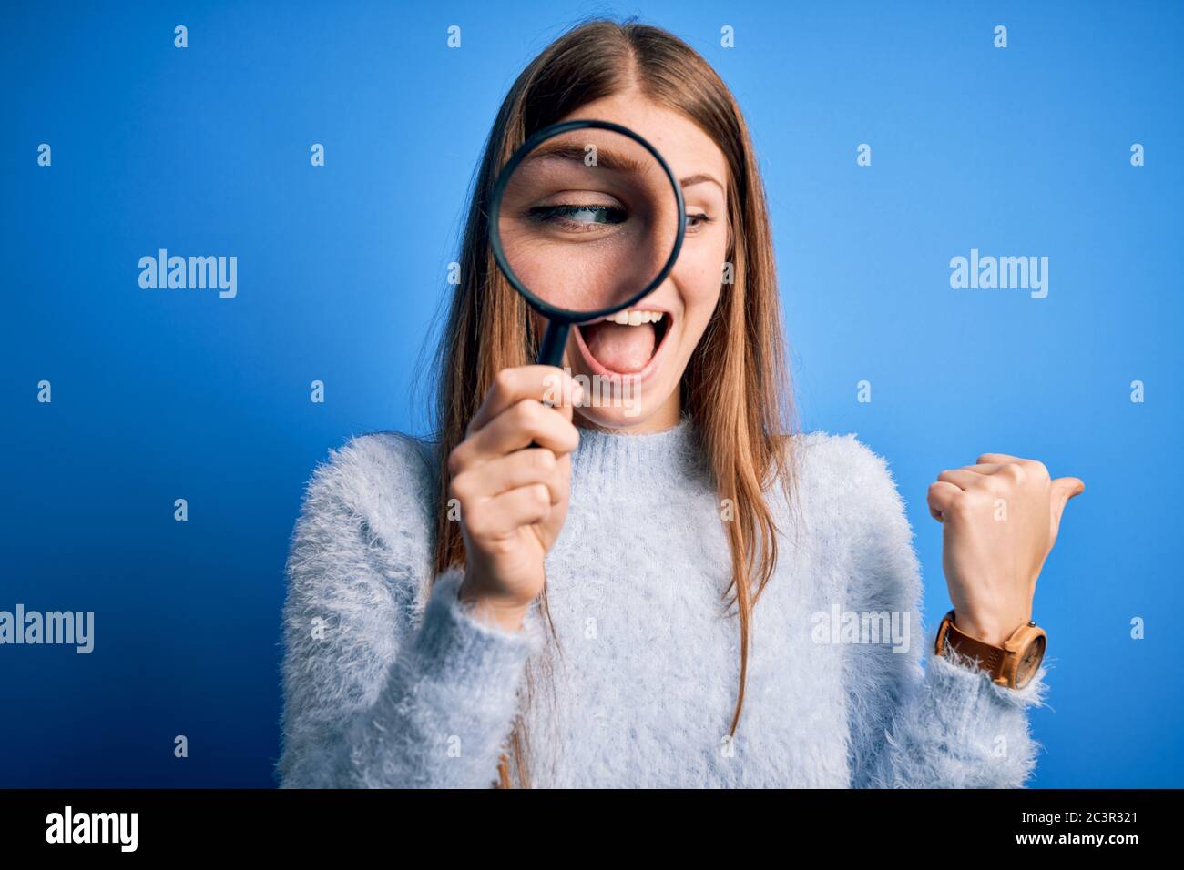 Young beautiful redhead detective woman using magnifying glass over ...