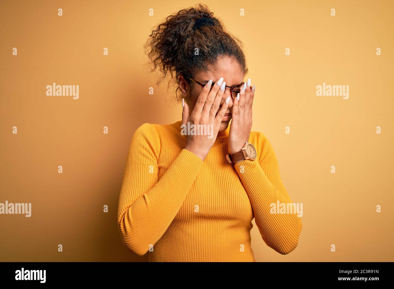 Young beautiful african american girl wearing sweater and glasses over yellow background rubbing eyes for fatigue and headache, sleepy and tired expre Stock Photo