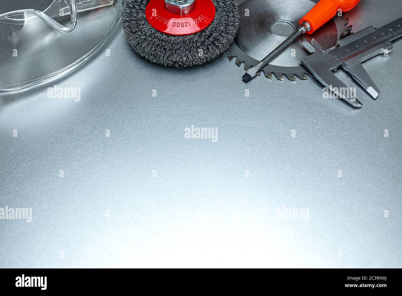 red abrasive steel brushes, circular saw blade, protective safety glasses and caliper on metal surface. tools for cleaning, polishing and cutting Stock Photo