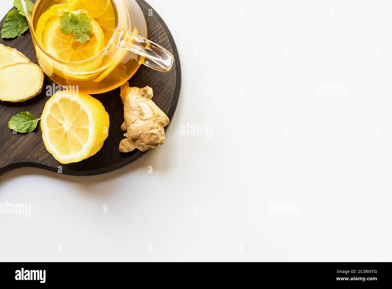 top view of hot tea in teapot served on wooden board with ginger root, lemon and mint on white background Stock Photo