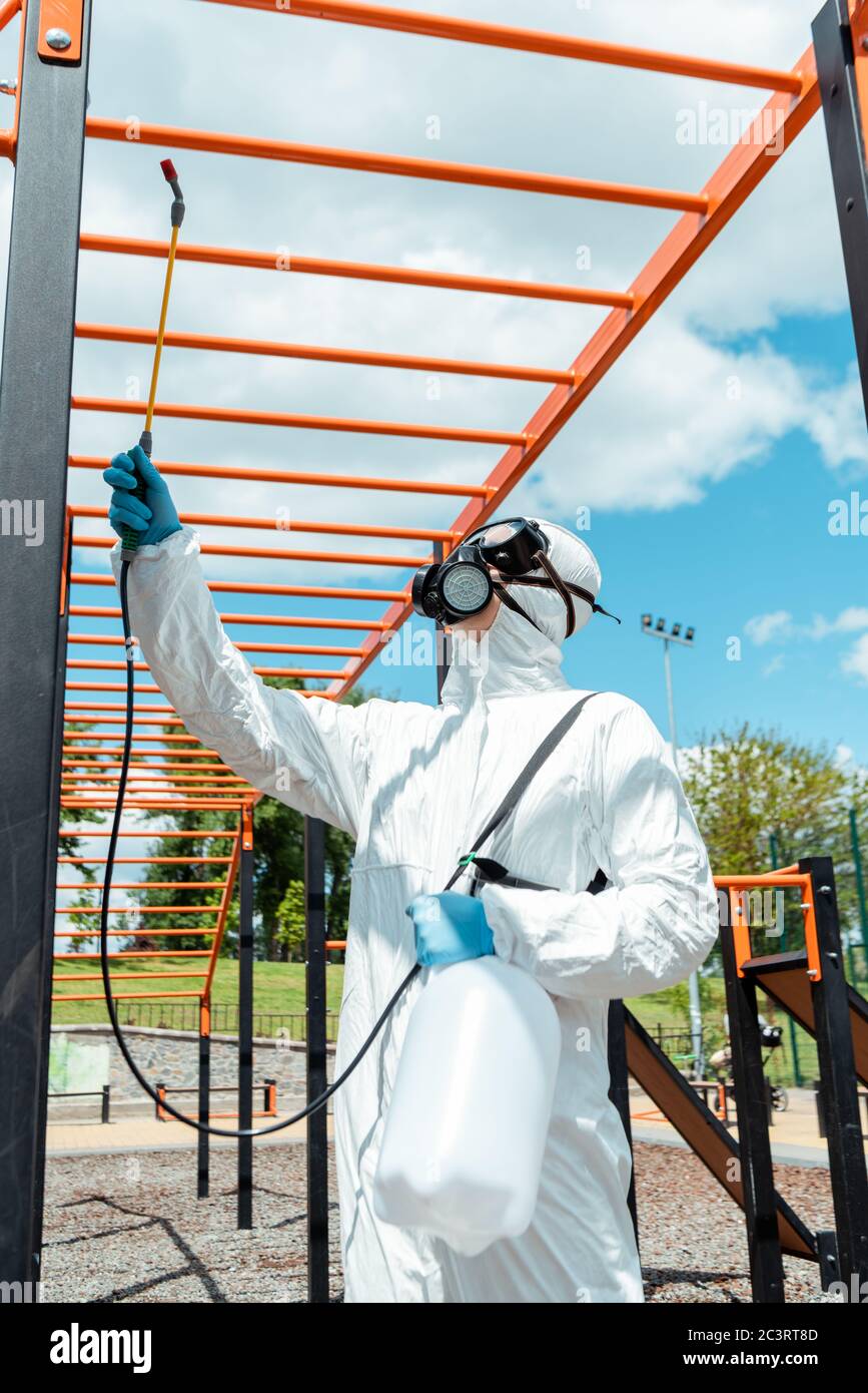 workman in hazmat suit and respirator disinfecting sports ground in park during covid-19 pandemic Stock Photo