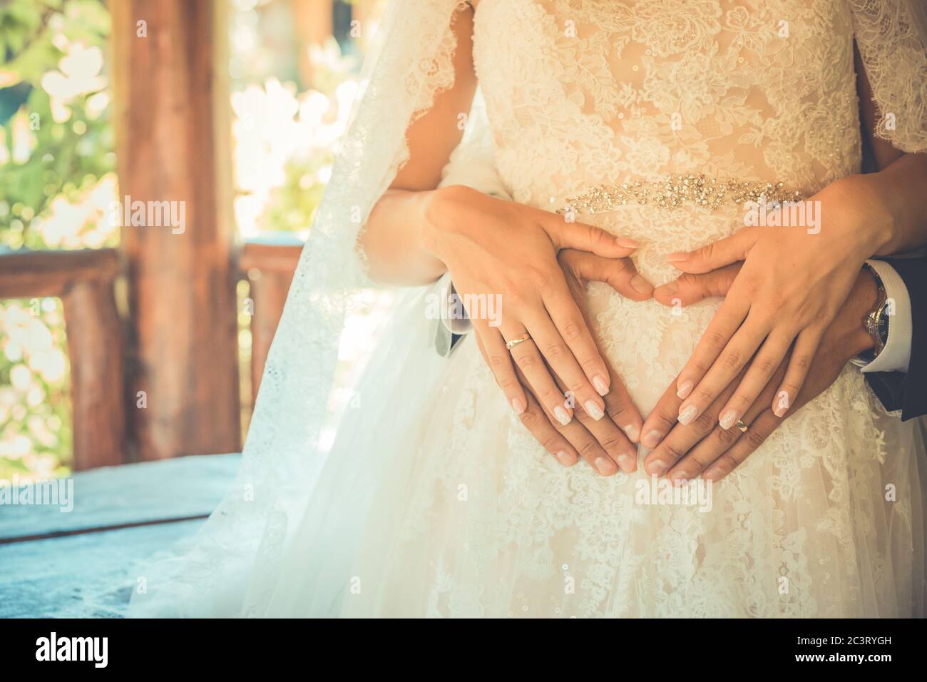 Four hands on belly of pregnant woman. Couple posing a hearts with their fingers on belly of expectant mother Stock Photo