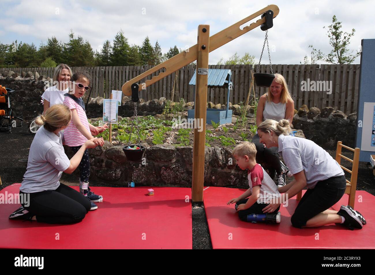(left to right) Kim McMaster alongside Specialist Physiotherapist Jenni Coulter and Oliver Cunningham with Specialist Physiotherapist Leah Honohan using the weighing scales during a shared theraplay session, watched by mums Kate McMaster (back left) and Michelle Cunningham, in the outside therapy area at the Craighalbert Centre. These sessions are taking place to deliver blended learning to children who are shielding. Coronavirus adaptations have been installed at the Scottish Centre for Children with Motor Impairments, Craighalbert Centre, Cumbernauld, as Scotland continues gradually lifting Stock Photo