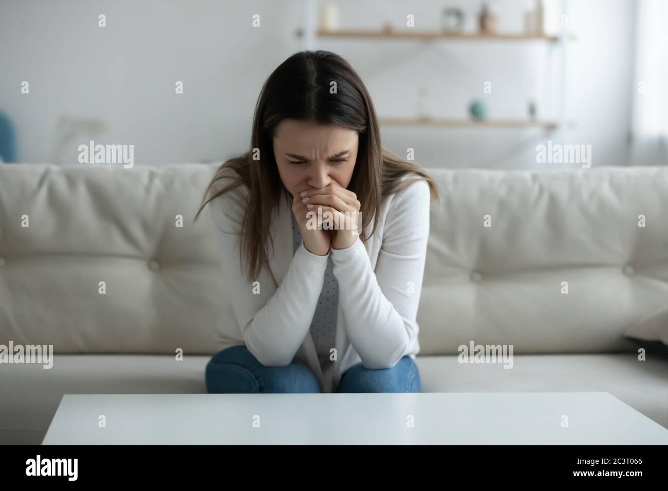 Depressed young woman crying seated on sofa alone at home Stock Photo
