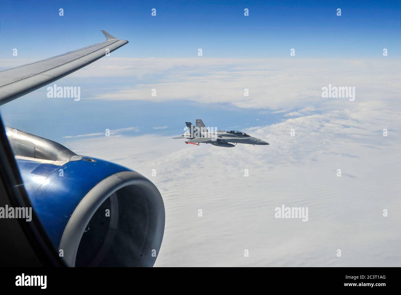 A view from inside passenger jetliner cabin of a military jet fighter escorting commercial aircraft at high altitude. Stock Photo