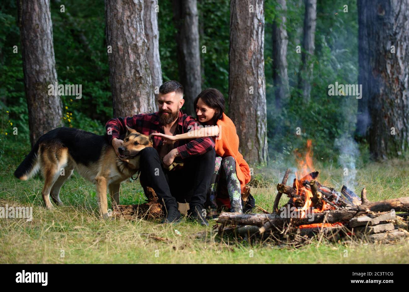 Let at læse Regeneration Maxim Man play, pat german shepherd dog near bonfire, nature background. Family  pet concept. Woman, man and dog on vacation, hiking. Couple in love or  young happy family spend time together Stock Photo -