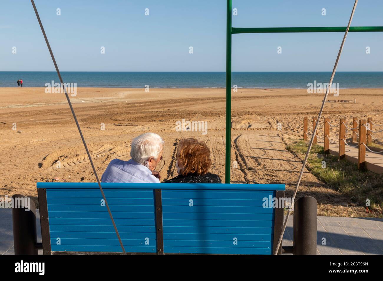 Elderly couple enjoying their time sitting on a bench overlooking the beach Porto Empedocle, Agrigento, Sicily, Italy Stock Photo