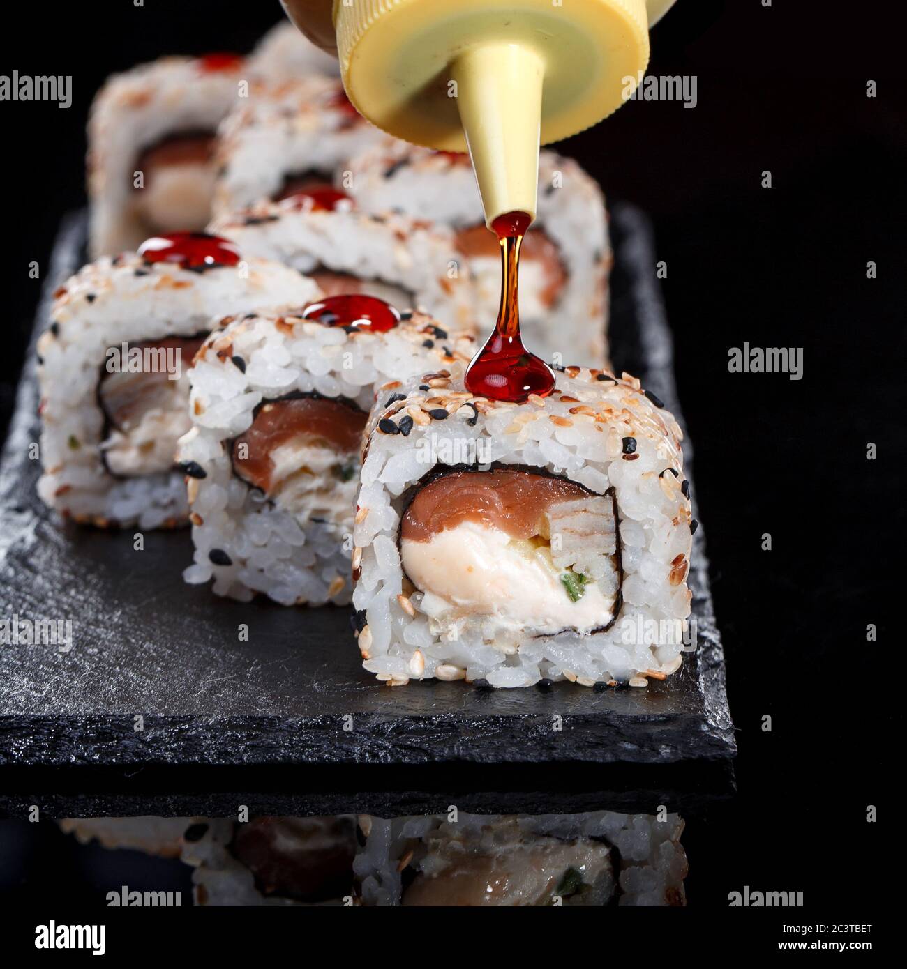 Delicious sushi roll served on black slate. In the frame, the hand of a chef pouring food with sweet sauce. Stock Photo