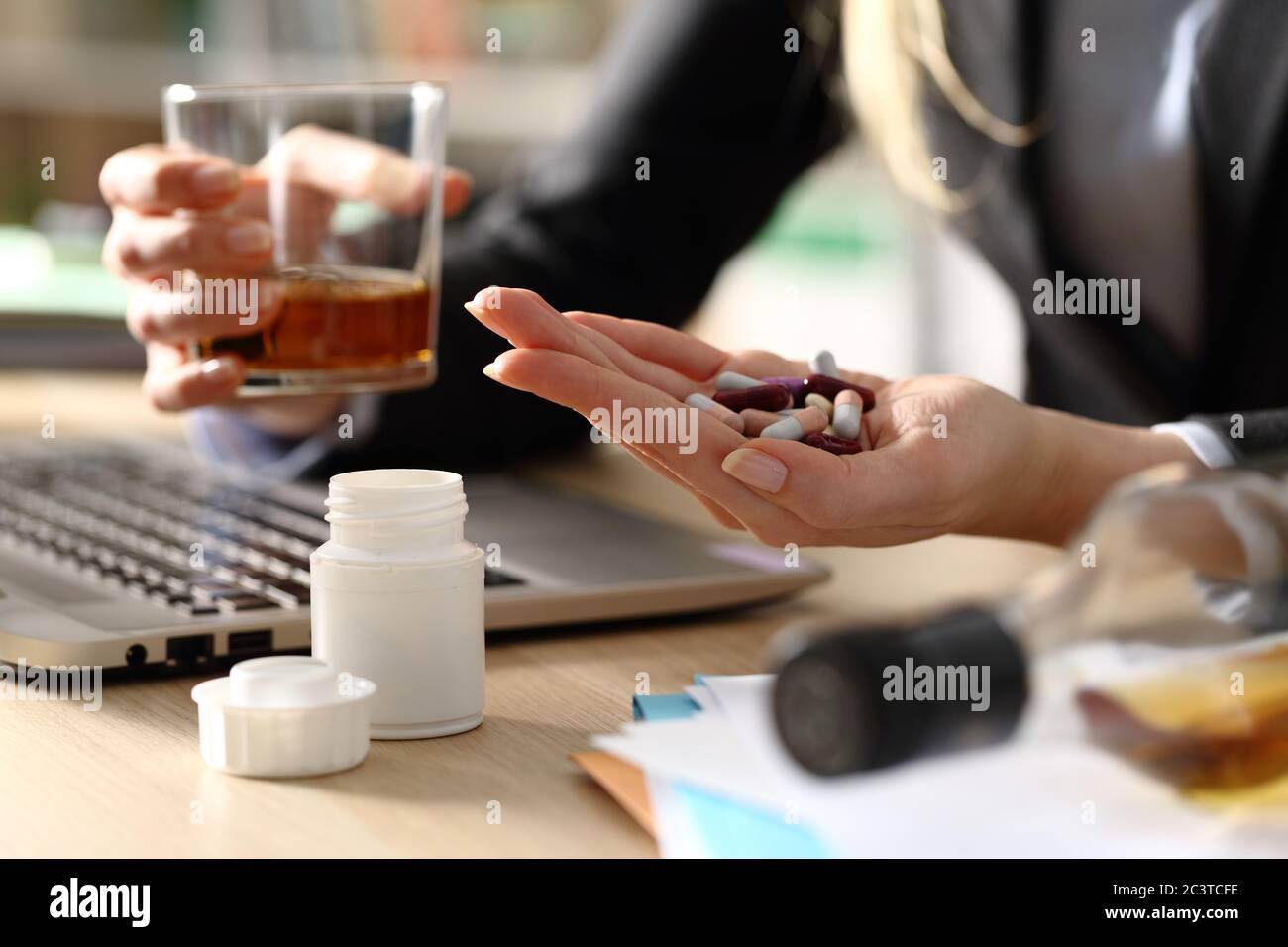 Close up of entrepreneur woman hands attempting suicide with pills and alcohol sitting on a desk at homeoffice Stock Photo