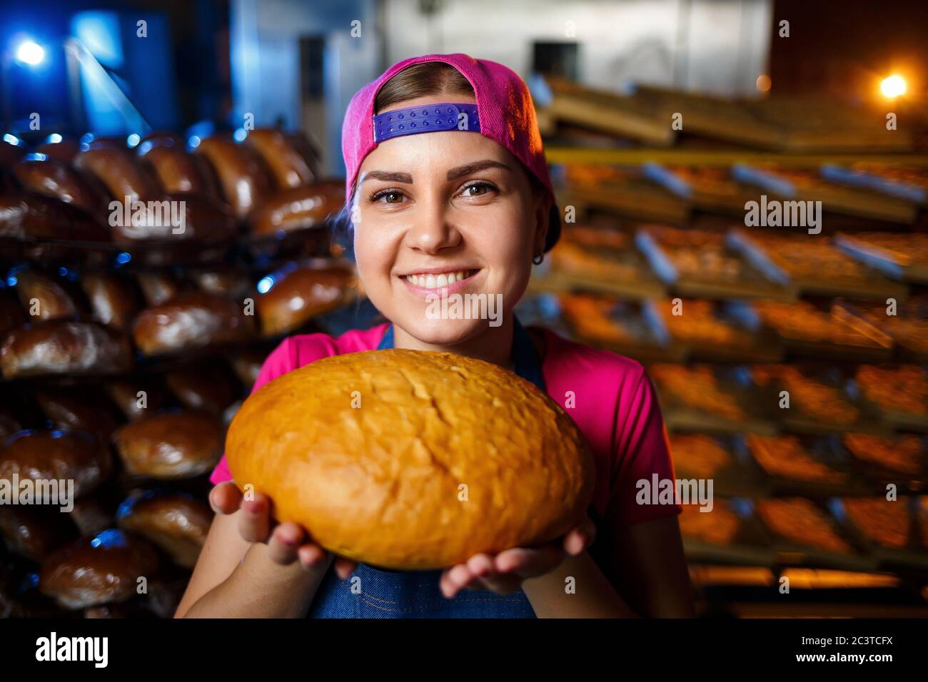 A baker woman holds fresh bread in her hand against the background of bakers  working in a bakery Stock Photo - Alamy