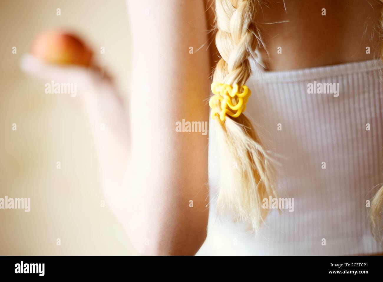 Young girl with blond pigtails in a white. Red apple in blurred hand. Stock Photo