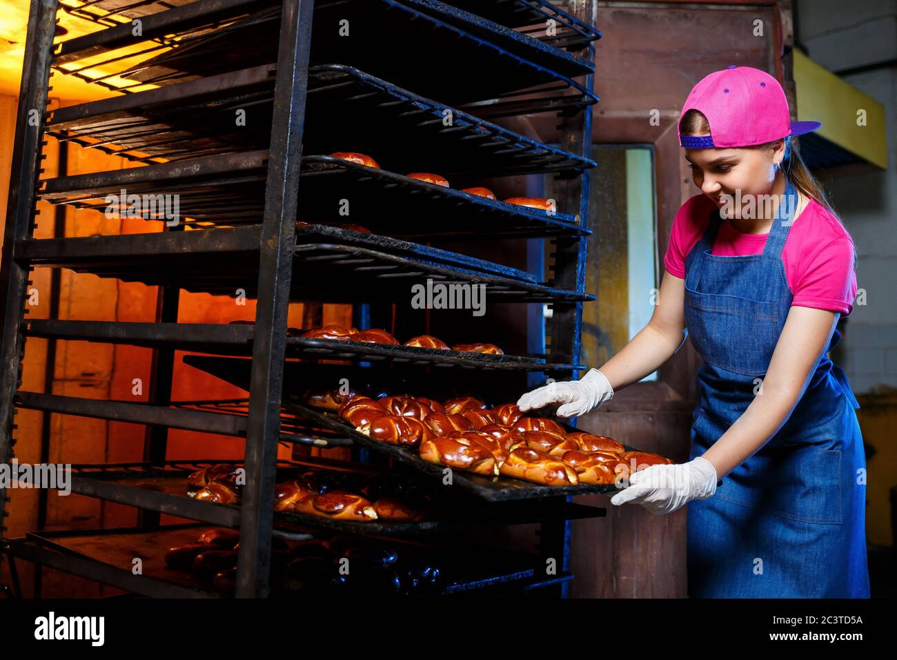 Young girl baker holds a tray with hot pastries against the background