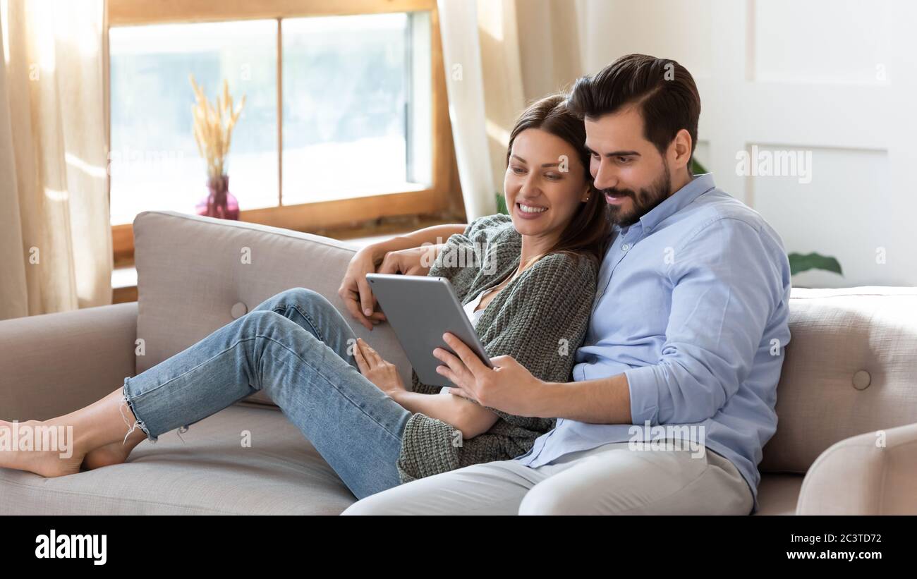 Happy young couple relaxing on couch, using computer tablet together Stock Photo