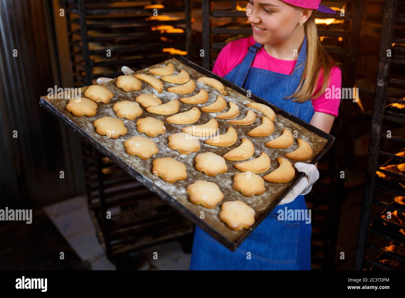 A professional baker girl is holding a tray with fresh cookies in her