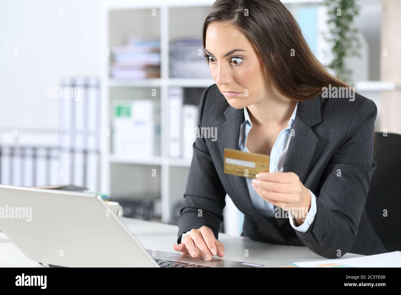 Perplexed executive woman pays online on laptop with credit card sitting on a desk at the office Stock Photo