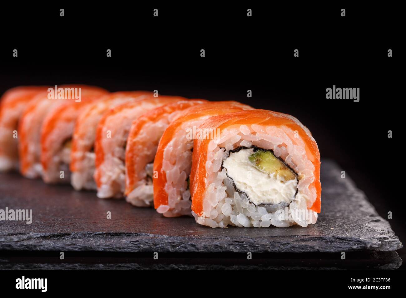 Philadelphia sushi rolls with salmon and cream cheese and avocado on a black slate plate close up. Stock Photo