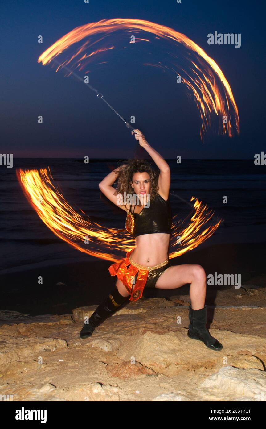 a female fire juggler juggles fire on the beach at