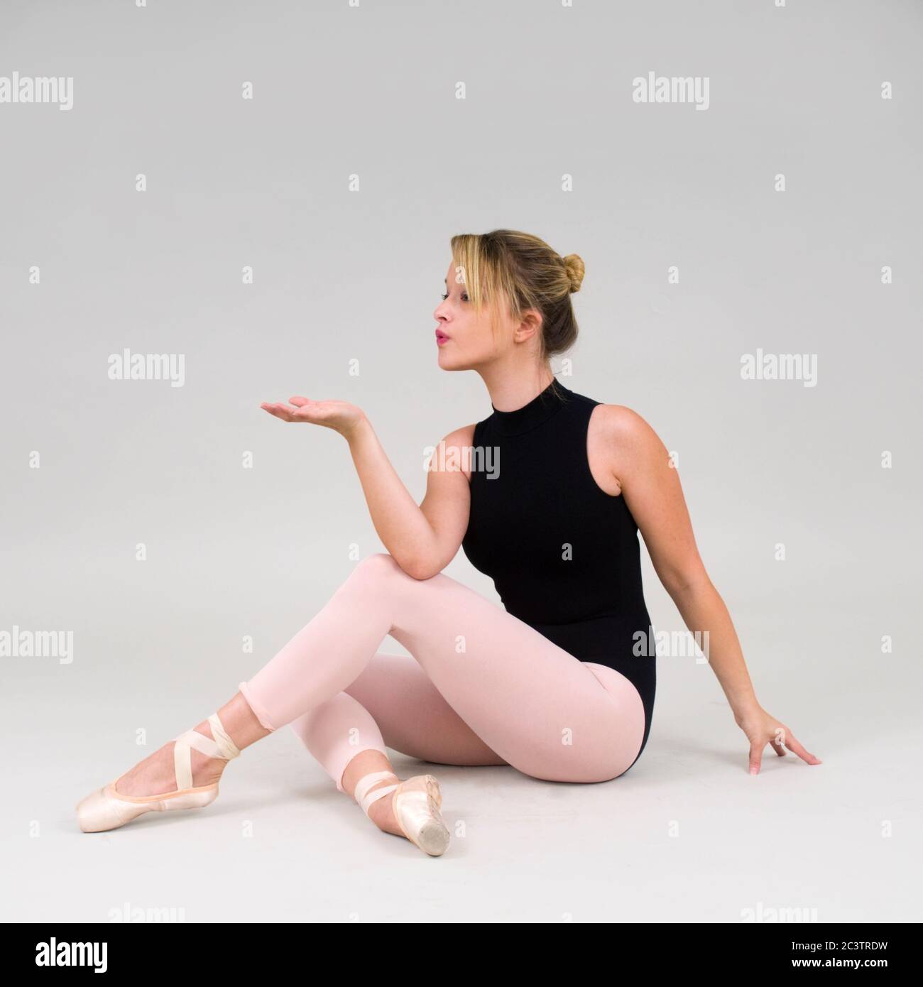 Female blond Ballet Dancer sits on floor and blows something out of her outstretched hand Stock Photo