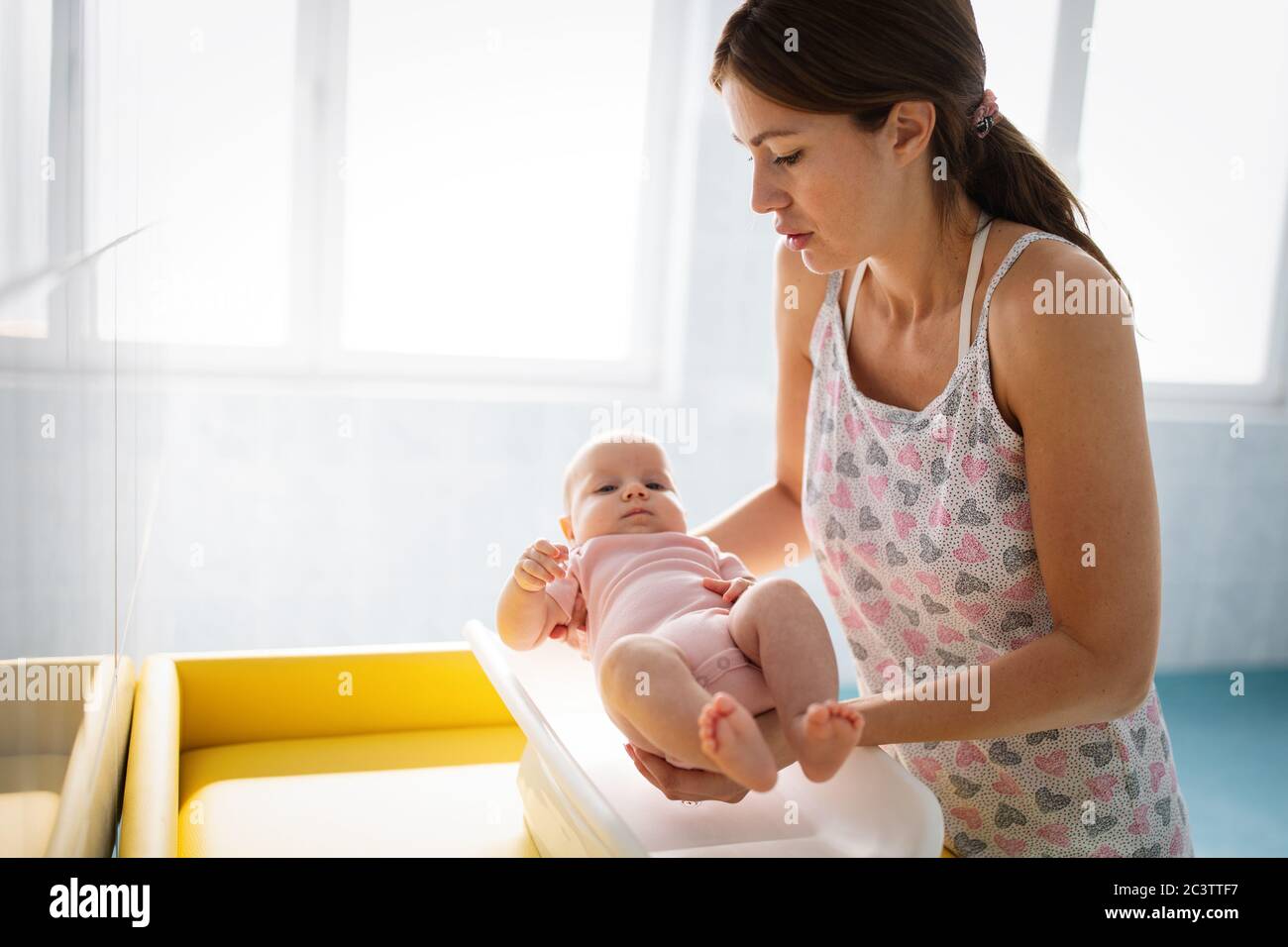 Beautiful young mother weighing little baby on scales Stock Photo