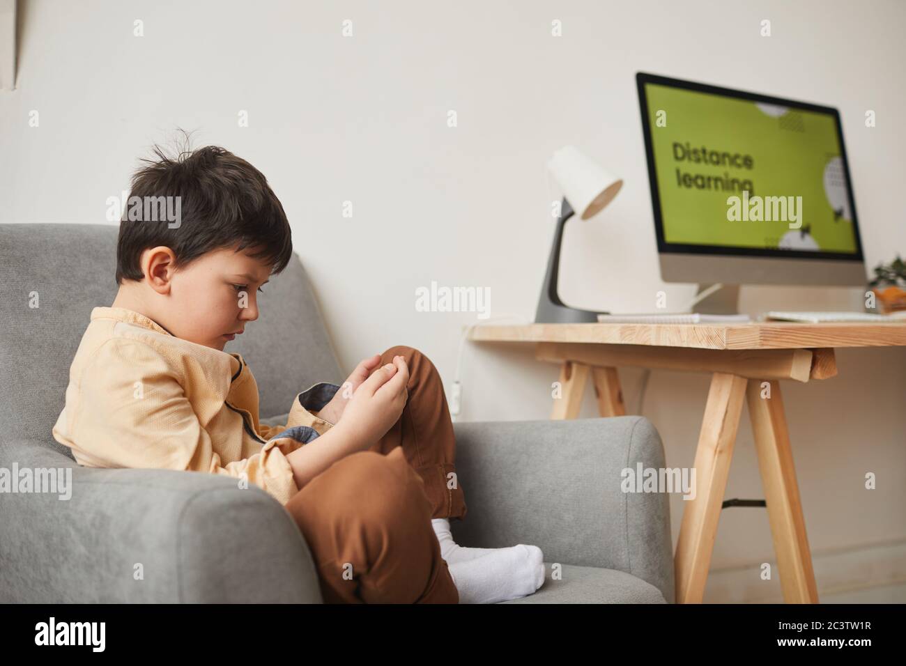 Side view portrait of cute boy sitting in armchair and using digital tablet with online school website in background, copy space Stock Photo