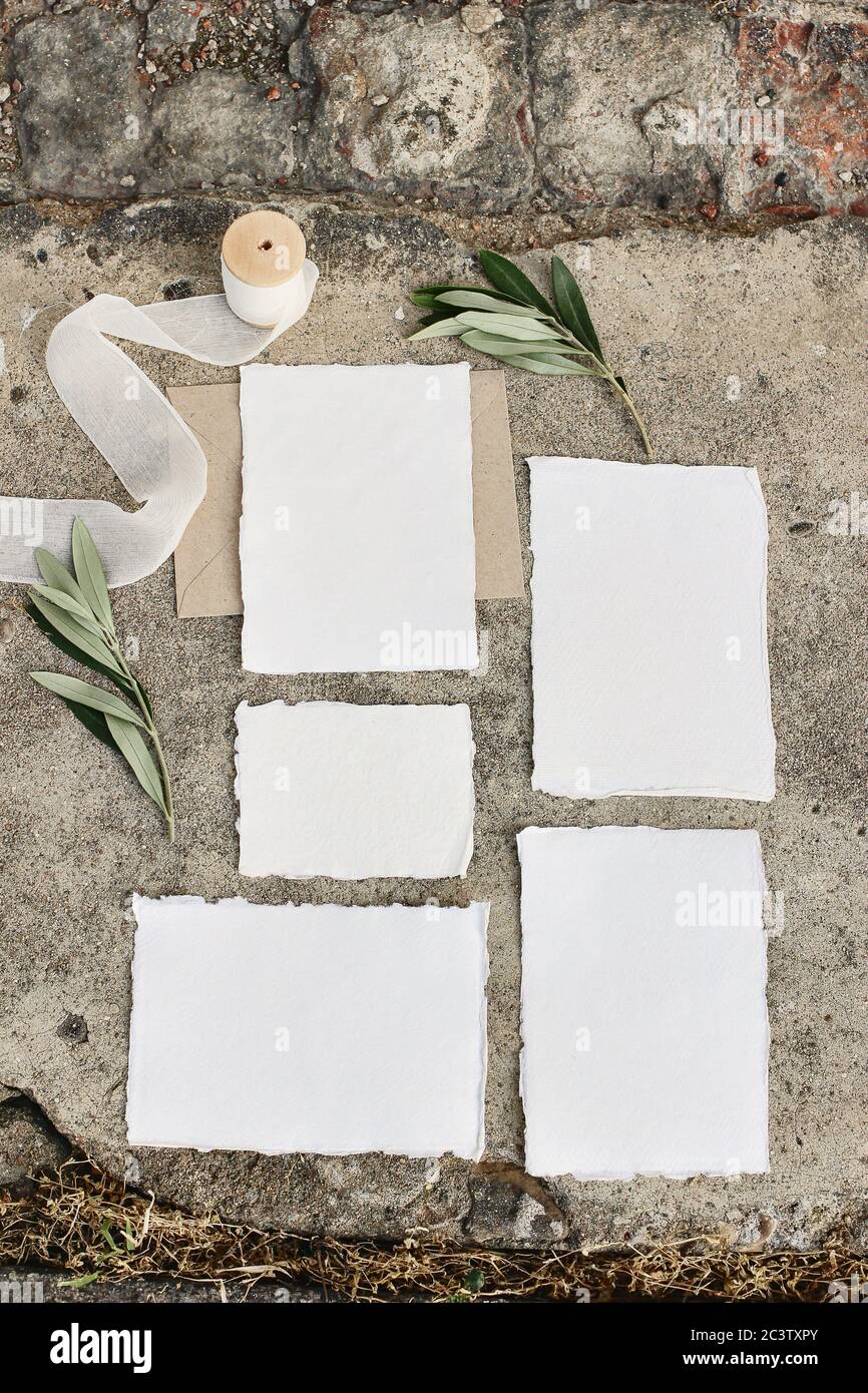 Summer wedding stationery mock-up scene. Blank greeting cards, envelopes, silk ribbon and olive branches on grunge concrete background.Vertical Stock Photo