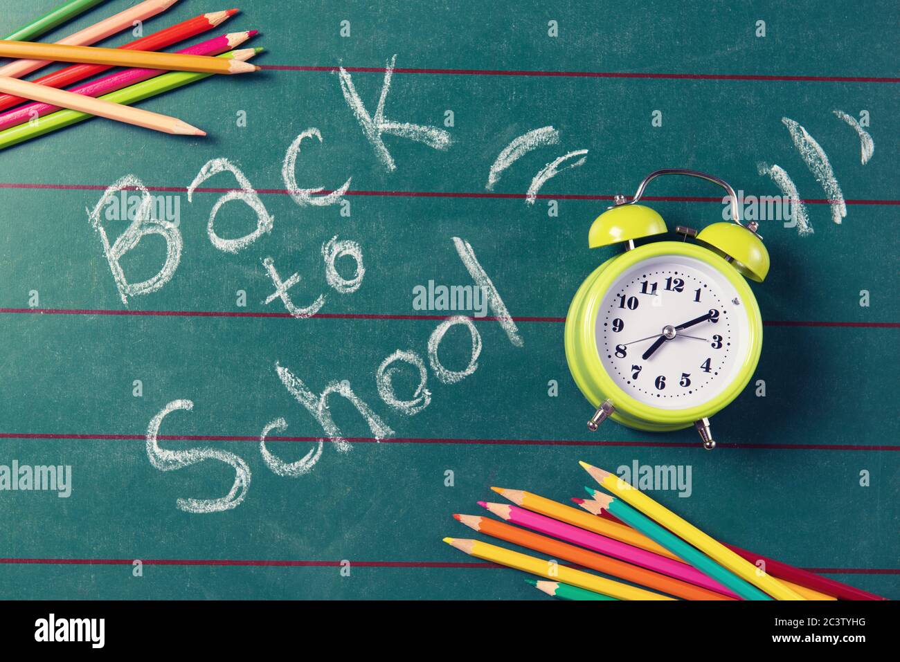 Green alarm clock and coloured pencils on the chalkboard with back to ...