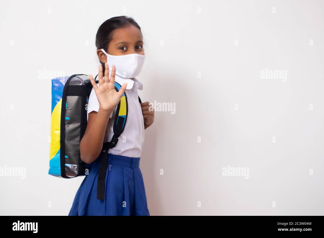 Happy child girl back to school after Covid-19 lock-down. Back to school concept waving good-bye to parents. Stock Photo