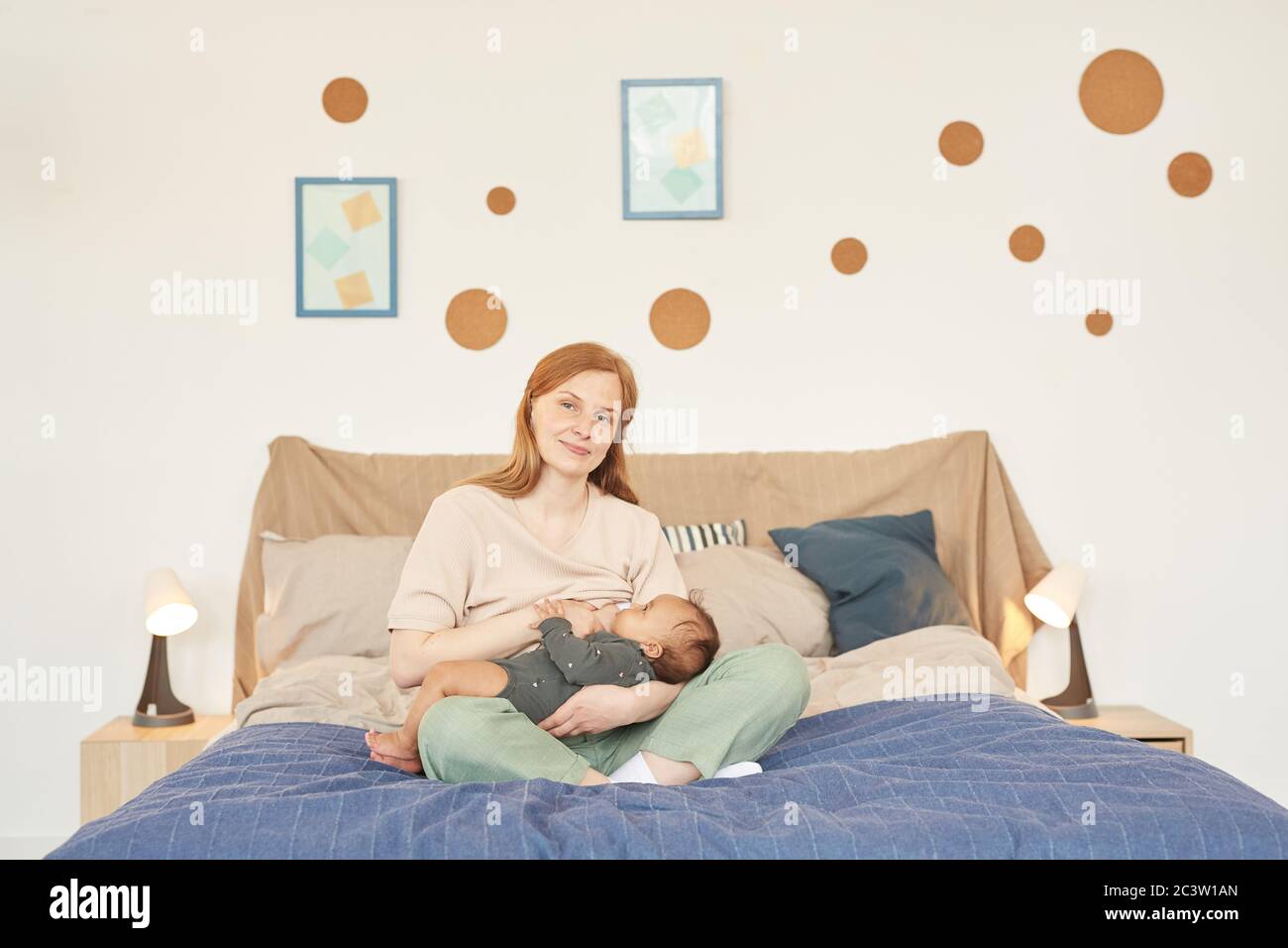 Warmtoned full length portrait of happy adult mother breastfeeding mixedrace baby and looking