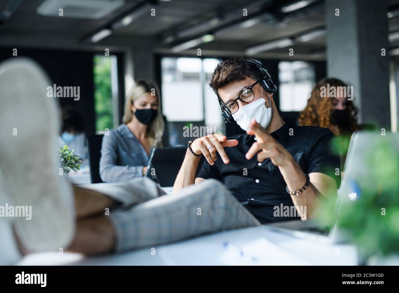 Young man with face mask back at work or school in office after lockdown, having fun. Stock Photo