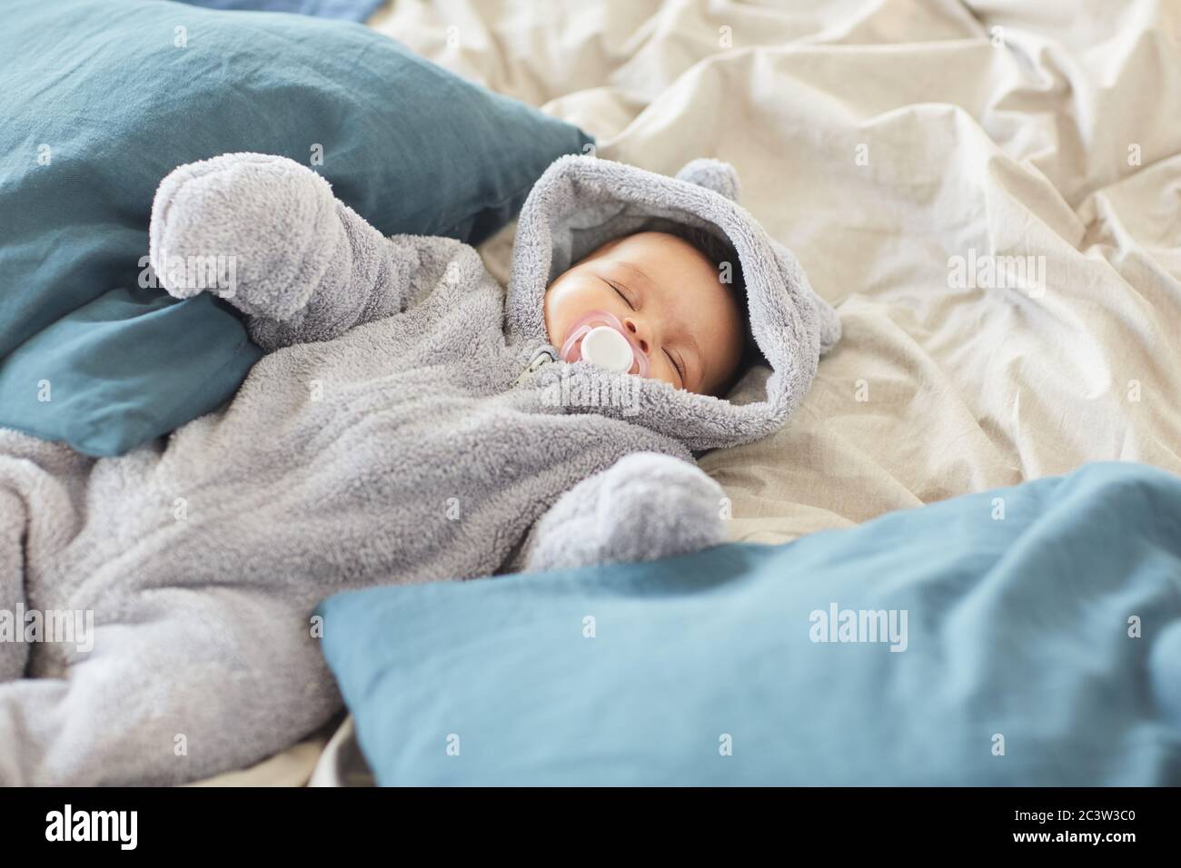 https://c8.alamy.com/comp/2C3W3C0/high-angle-portrait-of-cute-mixed-race-baby-wearing-fluffy-onesie-sucking-on-pacifier-while-sleeping-lying-on-bed-blankets-copy-space-2C3W3C0.jpg