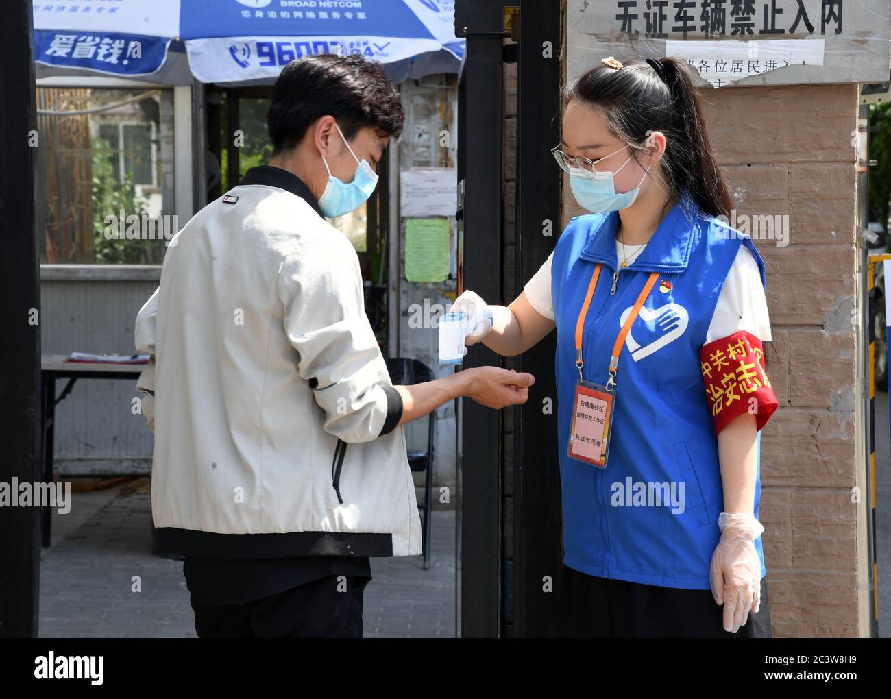 Beijing, China. 16th June, 2020. Volunteer Wang Yue (R) checks a resident's body temperature at the entrance of a community in Haidian District in Beijing, capital of China, June 16, 2020. Credit: Ren Chao/Xinhua/Alamy Live News Stock Photo