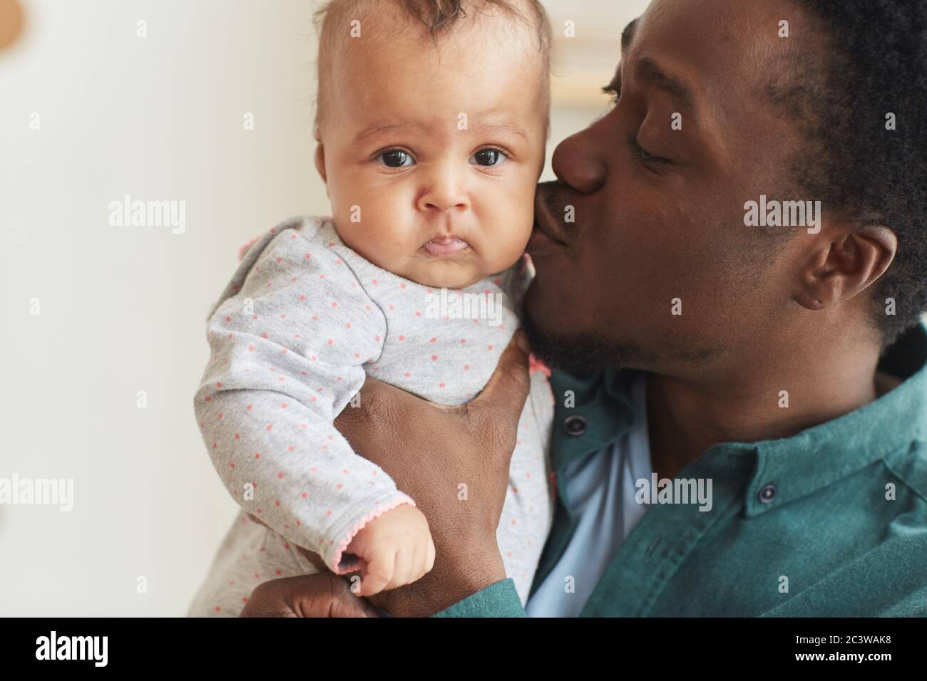 Close up portrait of happy African-American man kissing cute baby boy while holding him, copy space Stock Photo