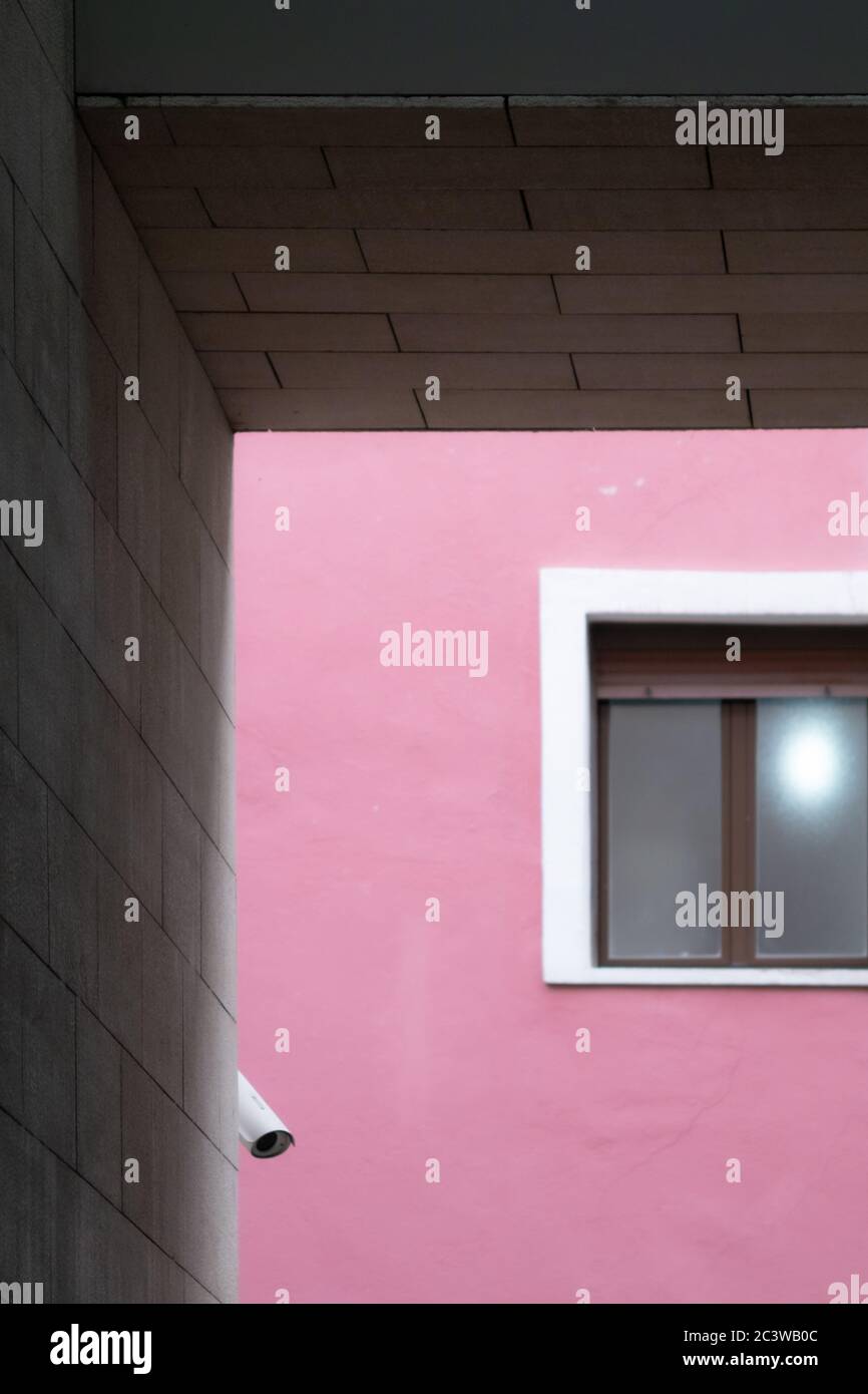 Composition of parallel and perpendicular lines with a window and a security camera on a magenta wall, framed with blocks of gray cement. Stock Photo