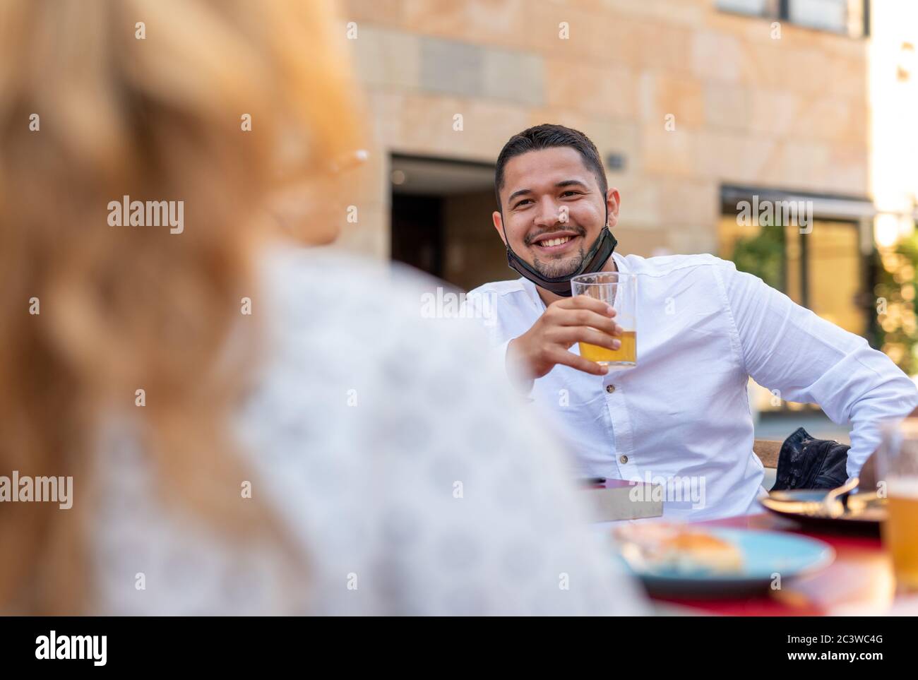 the new normality after the coronavirus epidemic, focus on the young man drinking a beer, wearing the protective mask under his chin and keeping socia Stock Photo