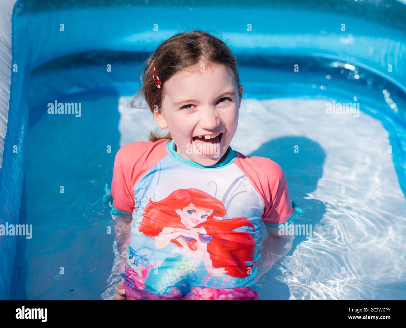 Little gir enjoys spalshing in a paddling pool in garden in summer