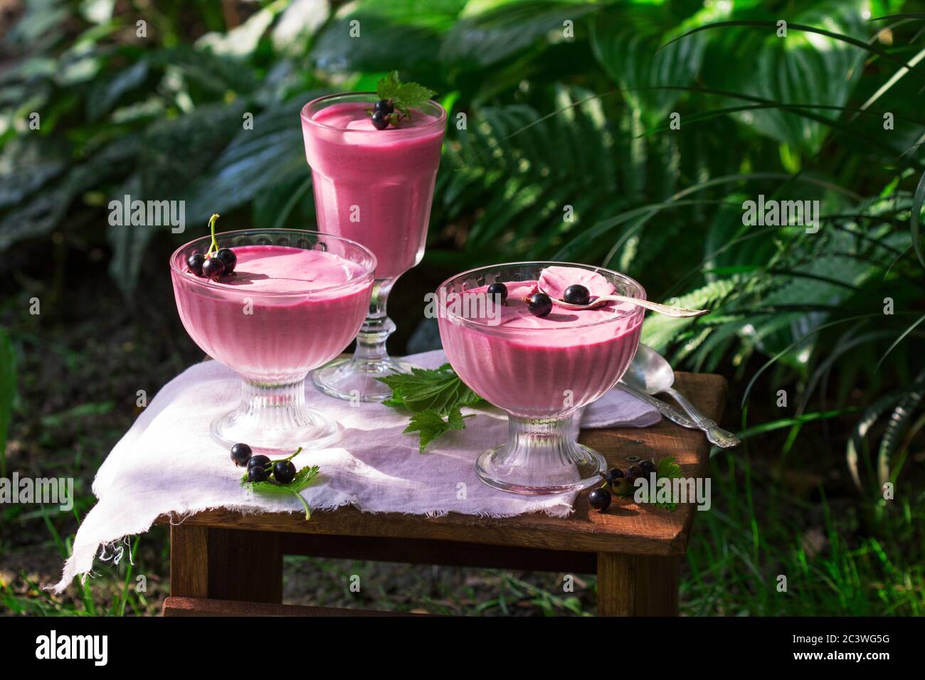 Berry mousse in glass vases on a wooden background in the garden. Stock Photo