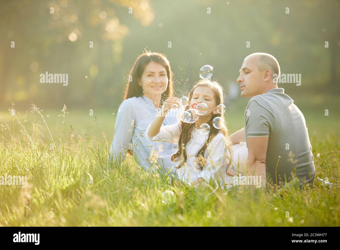 happy family with child girl blow soap bubbles together in park Stock ...