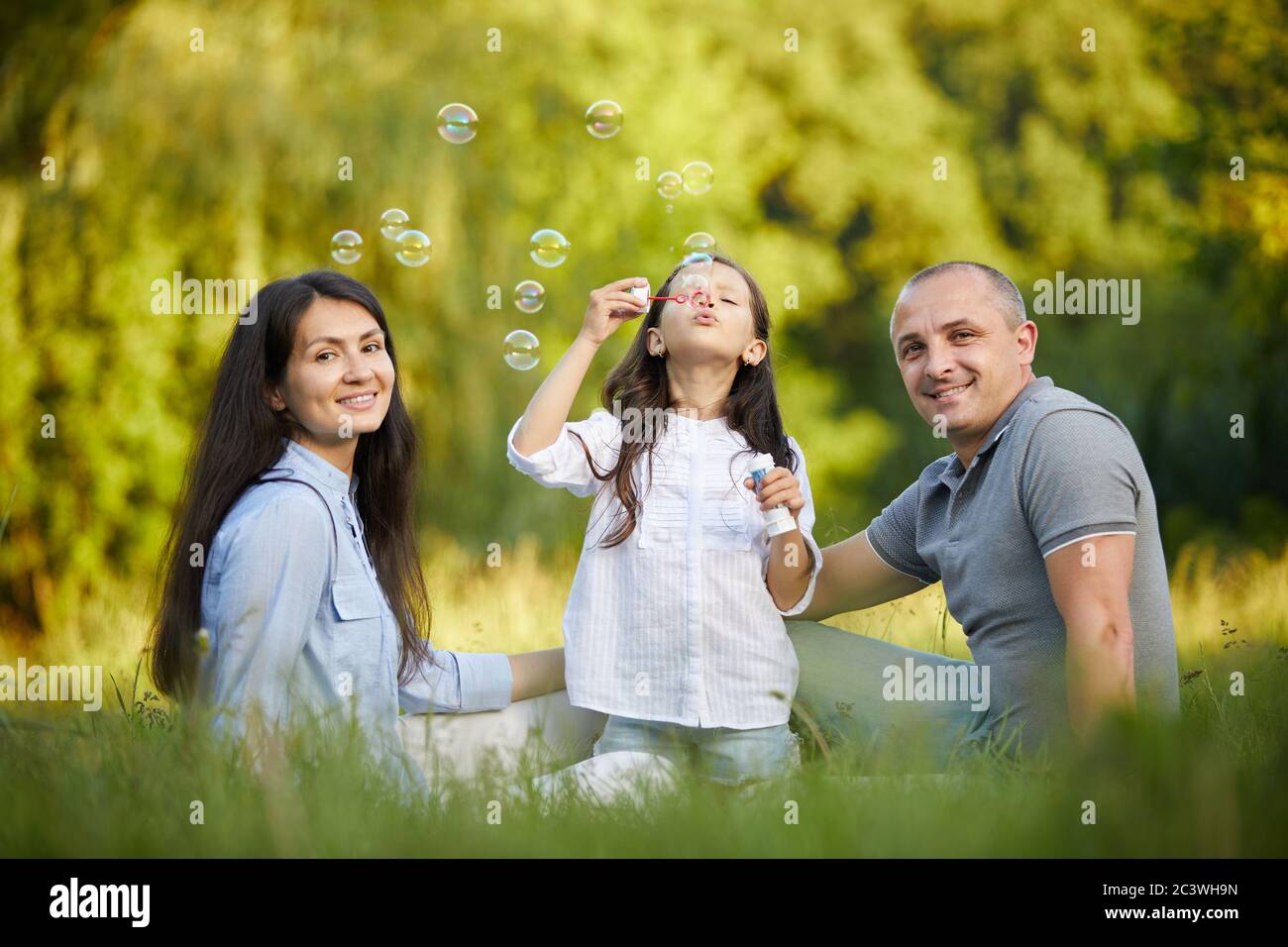 happy family with child girl blow soap bubbles in park Stock Photo - Alamy