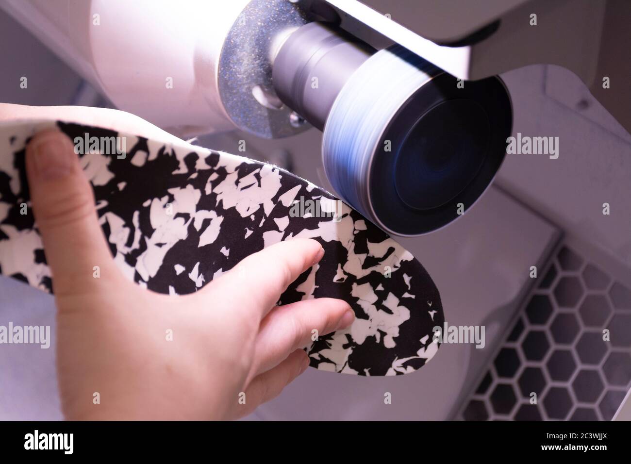 Hands of a unrecognizable female podiatrist preparing a black and white shoe insole on a sanding and polishing machine Stock Photo